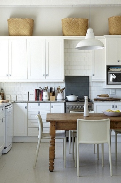 a chic neutral Scandinavian kitchen with vintage cabinets, a white tile backsplash, a rustic wooden table and pendant lamps