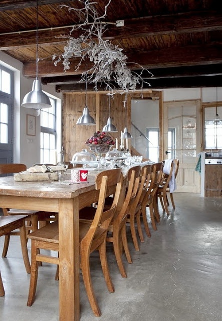 a rustic Scandinavian kitchen with a wooden dining set, whitewashed branches and silver pendant lamps plus a concrete floor