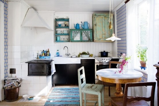 a modern meets vintage Scandi kitchen with black cabinets, a round table, mismatching chairs and shabby chic cabinets in bright colors