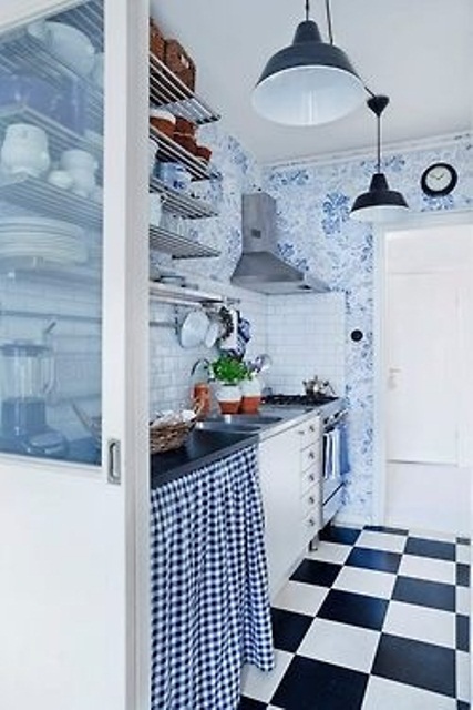 a retro kitchen with a checked floor, blue and white floral wallpaper, open shelves and pendant lamps
