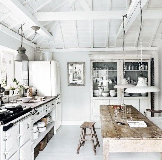 a white Nordic kitchen with a whitewashed buffet, pendant lamps, a rough wooden dining set