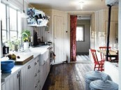 a rustic Scandinavian kitchen with white shiplap cabinets and whitewashed walls, red chairs and touches of blue here and there