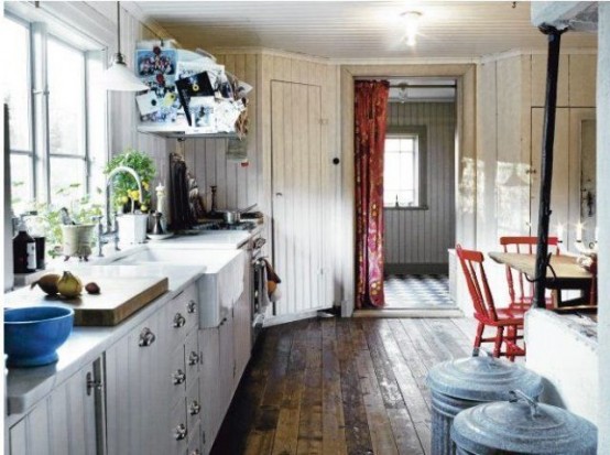 a rustic Scandinavian kitchen with white shiplap cabinets and whitewashed walls, red chairs and touches of blue here and there