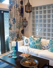 a sea-inspired living room with a light blue glass wall, a white sofa with printed pillows, a printed curtain and Moroccan lanterns