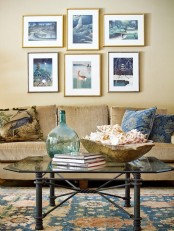 a modern beach living room with sandy walls, a gallery wall with sea-inspired artworks, a glass table and a tan sofa