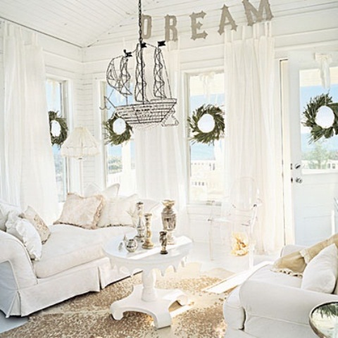 a white coastal living room with white furniture and curtains, a tan rug and a suspended ship