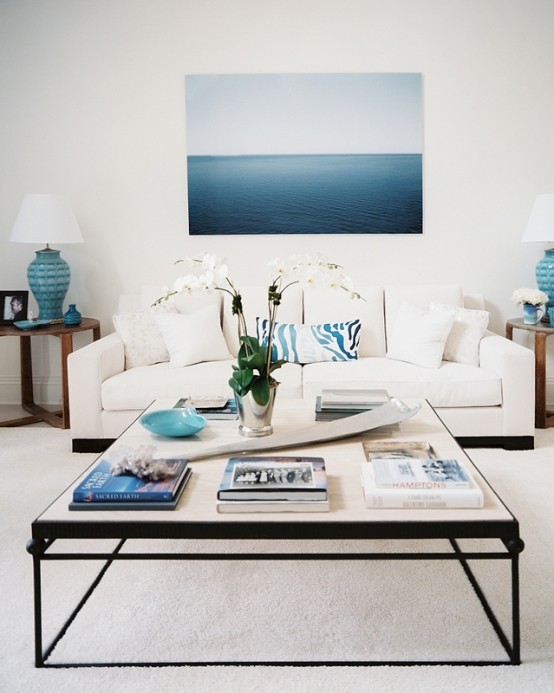 a beahcy living room in cremay and bold blues, a modern coffee table, a large and bold artwork, side tables with blue lamps