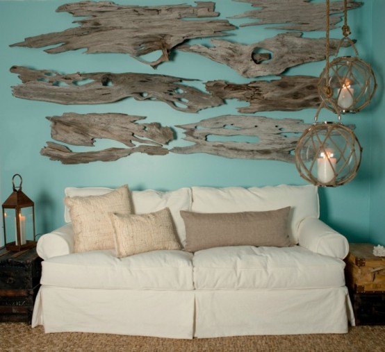 a beachy living room with a turquoise wall with driftwood, a white sofa and large glass candle lanterns