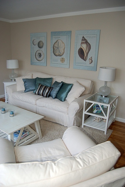 a neutral coastal living room with creamy furniture, a gallery wall of vintage sea posters, white tables