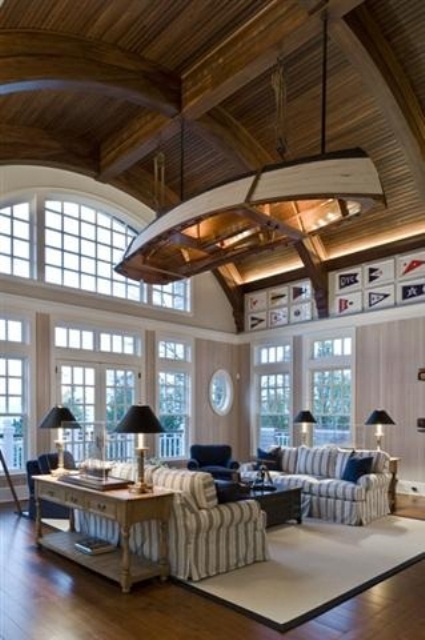 a coastal living room with a boat suspended over the space, striped and navy furniture and vintage lamps