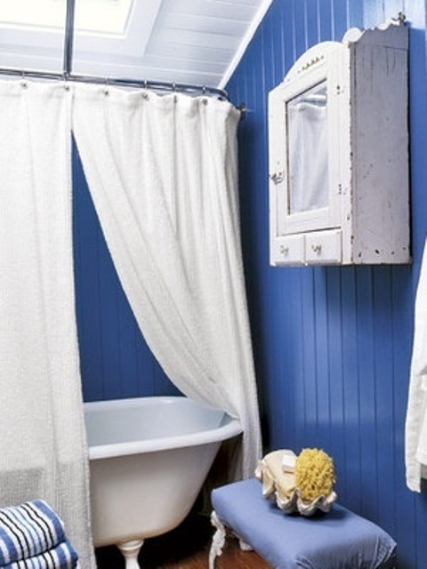 a bold blue and white bathroom with a neutral curtain, a shabby chic cabinet and a blue vintage stool