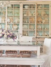 a gorgeous shabby chic dining room with a large shelving unit that takes a whole wall, shabby chic vintage furniture and a crystal chandelier