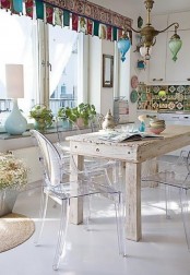 an eclectic dining room with a shabby chic table, ghost chairs, bright curtains, a chandelier and a bold tile backsplash