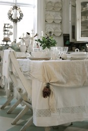 a cozy neutral shabby chic dining room with white walls and furniture, with layered tablecloths and simple white porcelain