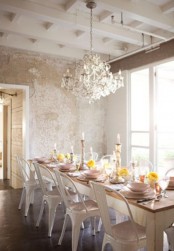 a shabby chic meets rustic dining room with a rustic table and metal chairs, a chic crystal chandelier and shabby chic walls