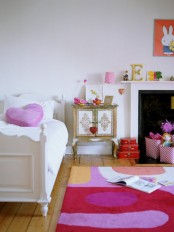 a colorful and whimsical girl’s room with a non-working fireplace, a bed, a pink heart pillow and a bold rug, a whimsical inlay cabinet and bold and colorful decor