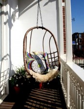 a small balcony with a suspended egg-shaped chair, potted plants and pillows is a welcoming nook to spend some time