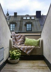 a small attic balcony with a built-in upholstered bench, pillows and a blanket and a potted flower is a cool space to get some sunshine