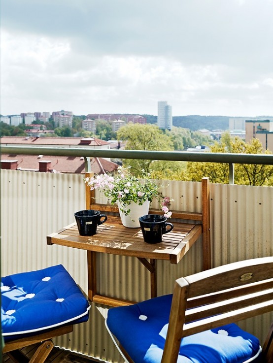 a small balcony with greenery, a folding table and chairs, bright cushions, is a great and cool space to be in