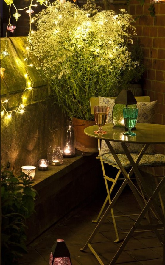 a small balcony with greenery, some folding furniture and string lights to add a bit of coziness and romance to the space