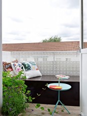 a small blacony with a storage daybed and bold pillows, potted greenery and a coffee table – choose durable outdoor fabric