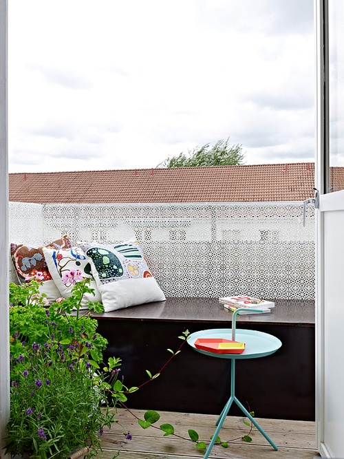 a small blacony with a storage daybed and bold pillows, potted greenery and a coffee table - choose durable outdoor fabric