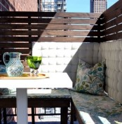 a cozy small balcony with a privacy screen, a corner bench with storage, some pillows and a coffee table is a lovely nook