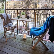 a small balcony with folding furniture – a table and chairs, a candle lantern and blankets to cozy up the space