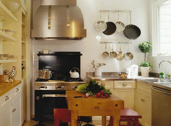 a warm-colored rustic kitchen wiht metal countertops, built-in cabinets and shelves, a large hood and a small table with red stools