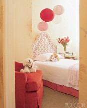 a small and lovely kid’s room with a red bed with neutral bedding, a red basket with toys, paper lamps in matching colors