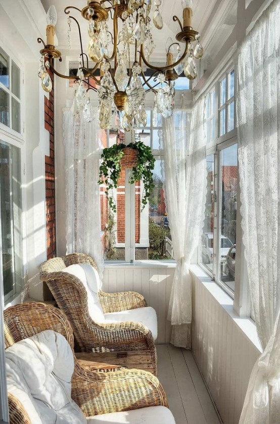 a vintage-inspired sunroom with a large crystal chandelier, lace curtains and wicker chairs