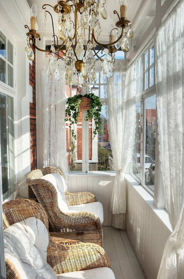 a vintage inspired sunroom with a large crystal chandelier, lace curtains and wicker chairs