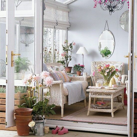 a traditional sunroom with white wicker furniture, printed and colorful textiles, lamps, mirrors and potted flowers