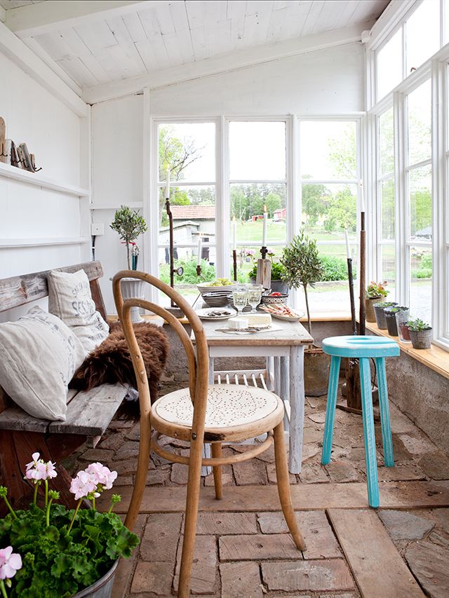 a vintage Scandianvian sunroom with a comfy bench and a long windowsill with potted blooms and greenery and a dining table of wood