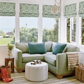 a refreshing sunroom nook with green shades and furniture, comfy ottomans and colorful touches