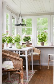 a sunroom with a meal space of a white table and wicker chairs and lots of potted flowers