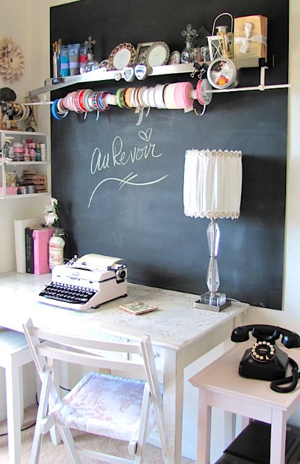 a vintage home office with a vintage desk and a couple of chairs, a chalkboard accent wall, a wall-mounted shelf and an additional one with jewelry