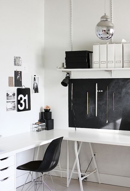 a laconic black and white Scandinavian home office with a white corner desk, a mini gallery wall, a wall-mounted shelf and a chalkboard for leaving notes and marks