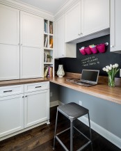 a home office in the kitchen, with white cabinets around, a floating desk, a metal stool, a chalkboard accent wall for notes