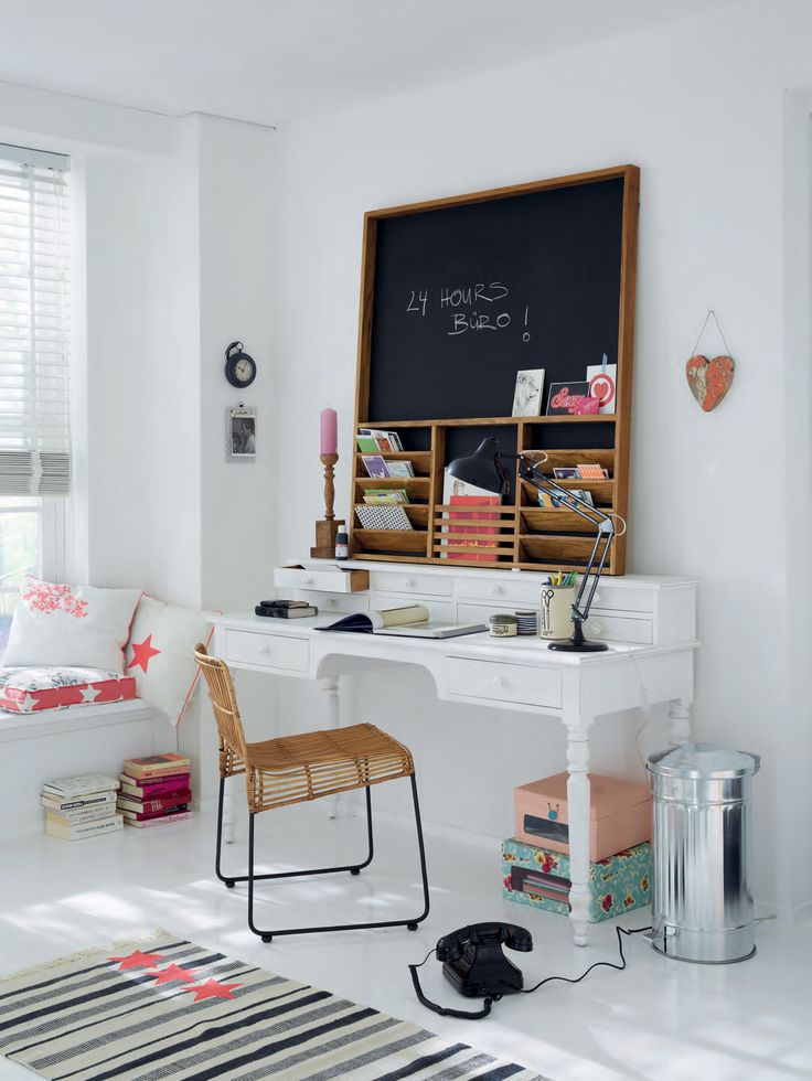 a cute and welcoming white home office with a windowsill with pillows, a white desk, a rattan chair and a chalkboard in a frame for chalking notes