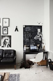 a Nordic black and white home office with a small black desk and a black leather sofa, a white chair, a chalkboard and some black and white artworks