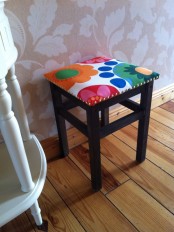 an IKEA Oddvar stool painted dark and upholstered with bright fabric and with decorative nail trim