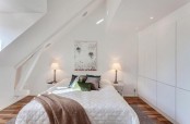 a tiny white bedroom with sleek white cabinets, built-in lights, a bed and lamps and much natural light