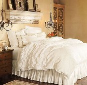 a neutral shabby chic bedroom with buttercream colored walls, a small shelf, a bed with pretty ruffle bedding and mismatching nightstands
