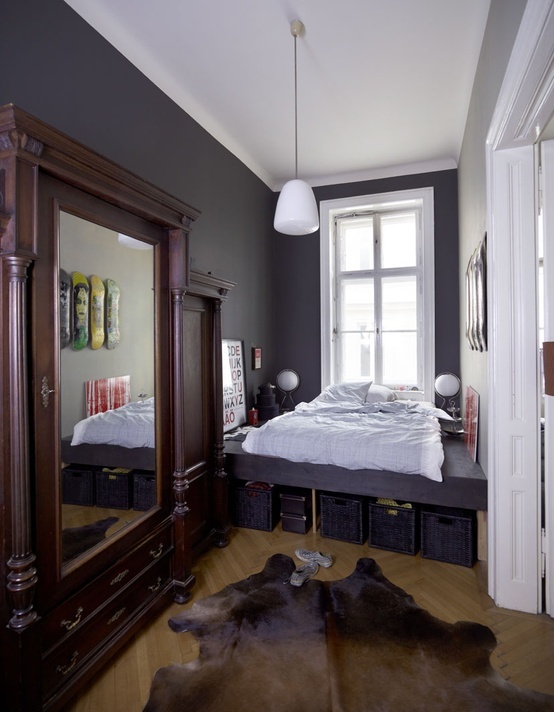 a small eclectic bedroom with graphite grey walls, a built-in bed with storage and wardrobes with mirror doors