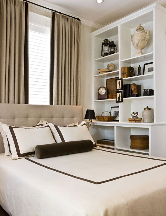 a small neutral bedroom with style, with a large wall storage unit, a neutral upholstered bed and neutral curtains