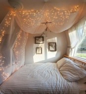 a tiny neutral bedroom with a large bed, artworks and a canopy with lights and a large window