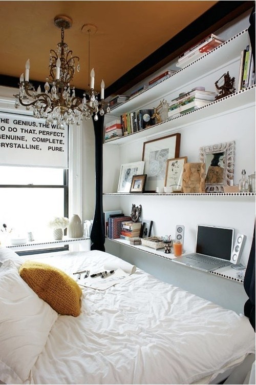 a tiny eclectic bedroom with a large wall storage unit, a large bed, a crystal chandelier and a windowsill desk