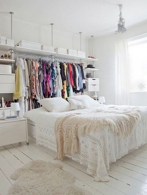 a small white bedroom with a makeshift closet, a bed and some closed storage units plus much natural light