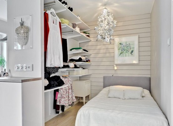 a tiny bedroom with a whitewashed wooden wlal, a bed, a makeshift closet, a catchy chandelier over the space